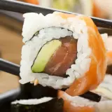 Palillos sostienen un rollo de sushi con salmón y aguacate. ¡Cuidado, el sushi engorda si no te controlas!