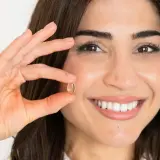 Mujer sonriente muestra una cápsula de omega 7, un aliado para quienes buscan adelgazar de forma natural.