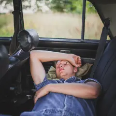 Joven descansando en el asiento trasero de un coche, demostrando que se puede dormir en el coche.