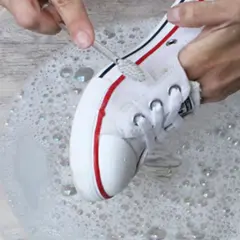 Manos limpian zapatillas blancas de tela con un cepillo en agua con jabón.