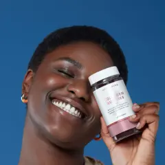 Mujer sonriente con un frasco de gomitas de colágeno para la piel, que prometen una piel radiante.