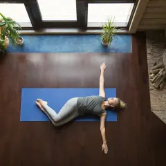 Mujer realizando ejercicios de espalda en casa, estirando su cuerpo sobre una esterilla azul.