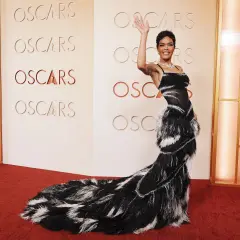 Una mujer saluda en la alfombra roja de los Oscars, luciendo un espectacular vestido negro con plumas.
