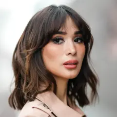 Mujer con un moderno corte wolf cut, cabello castaño ondulado y maquillaje llamativo.