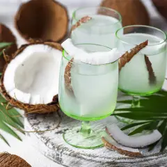 Refrescante agua de coco servida en copas verdes, decoradas con trozos de coco y hojas de palma.