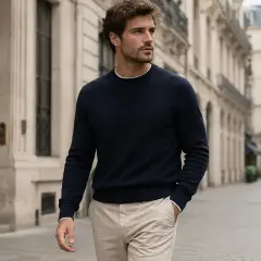 Hombre con jersey azul marino y pantalones beige camina por una calle parisina.