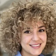 Sonrisa radiante de una mujer con un voluminoso flequillo pelo rizado rubio.