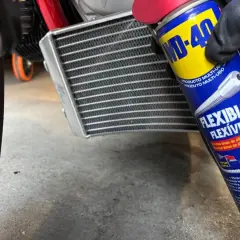 Mano enguantada usa spray WD-40 para limpiar radiador coche.