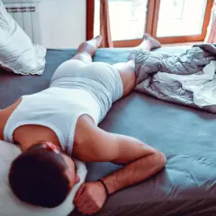 Hombre durmiendo en la cama, con una camiseta blanca y pantalones cortos. Se siente cómodo, es bueno dormir sin ropa interior.