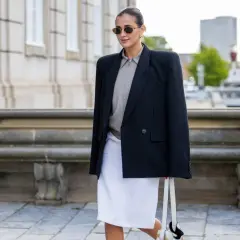Mujer con blazer negro, falda blanca y bolso, un look que se lleva este otoño.