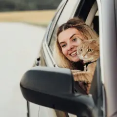 Mujer sonriente con un gato naranja en el coche. Consejos para saber como tranquilizar a un gato en el coche y que disfrute del viaje.