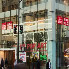 Edificio de cristal con letreros rojos de UNIQLO. La tienda, de origen japonés, se encuentra en una calle concurrida.