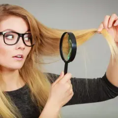 Mujer con gafas examina su cabello rubio con lupa, preocupada porque no me crece el pelo.