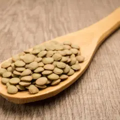 Cuchara de madera llena de lentejas verdes. Aunque las lentejas engordan, son una fuente de proteína y fibra.