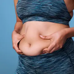 Mujer de 50 años se pellizca el abdomen, buscando perder grasa abdominal.