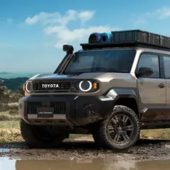 Un Toyota Land Cruiser FJ listo para la aventura, con equipo de campamento en el techo, avanza por un camino embarrado en un paisaje tropical.