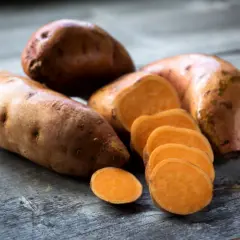 Boniato entero y en rodajas sobre madera. Descubre los beneficios del boniato para adelgazar y una dieta saludable.