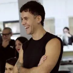 Luis de Javier diseñador, sonriente y con los brazos cruzados, rodeado de gente en un taller.