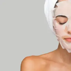 Mujer aplicándose mascarillas hidratantes pelo, con toalla en la cabeza.