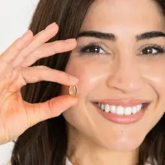 Mujer sonriente muestra una cápsula de omega 7, un aliado para quienes buscan adelgazar de forma natural.