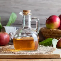Botella de vidrio con vinagre de sidra de manzana, rodeada de manzanas rojas y verdes frescas.