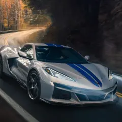 Un deportivo plateado con franjas azules recorre una carretera sinuosa entre árboles. Podría ser el mejor coche del mundo.
