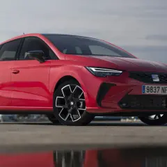 Un Seat Ibiza rojo vibrante, uno de los modelos más icónicos, posa con estilo frente a un paisaje urbano.