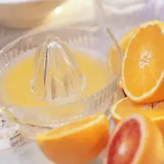 Exprimiendo naranjas frescas en un exprimidor de vidrio. El zumo de naranja natural recién hecho, listo para disfrutar.