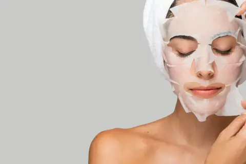 Mujer aplicándose mascarillas hidratantes pelo, con toalla en la cabeza.