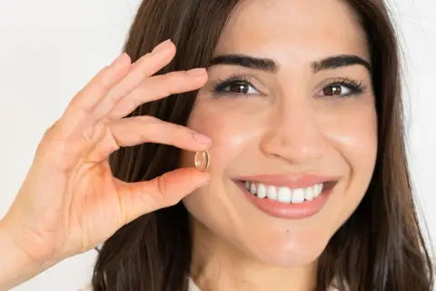 Mujer sonriente muestra una cápsula de omega 7, un aliado para quienes buscan adelgazar de forma natural.