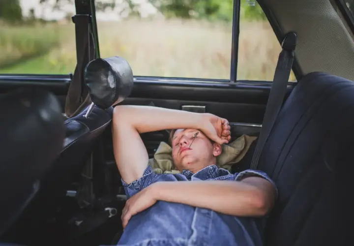 Joven descansando en el asiento trasero de un coche, demostrando que se puede dormir en el coche.