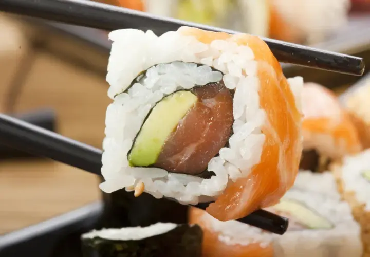 Palillos sostienen un rollo de sushi con salmón y aguacate. ¡Cuidado, el sushi engorda si no te controlas!