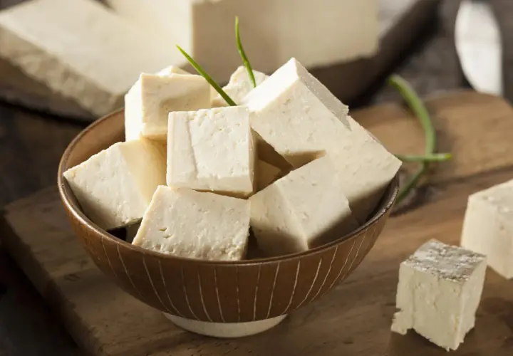 Tofu en cubos en un tazón, con bloques enteros al fondo. Aunque dicen que el tofu engorda, es un alimento versátil.