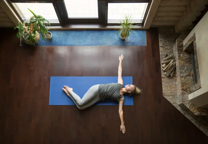 Mujer realizando ejercicios de espalda en casa, estirando su cuerpo sobre una esterilla azul.