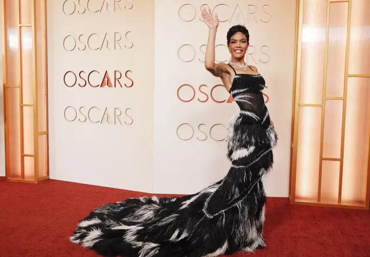 Una mujer saluda en la alfombra roja de los Oscars, luciendo un espectacular vestido negro con plumas.