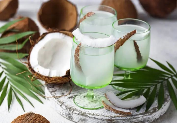 Refrescante agua de coco servida en copas verdes, decoradas con trozos de coco y hojas de palma.