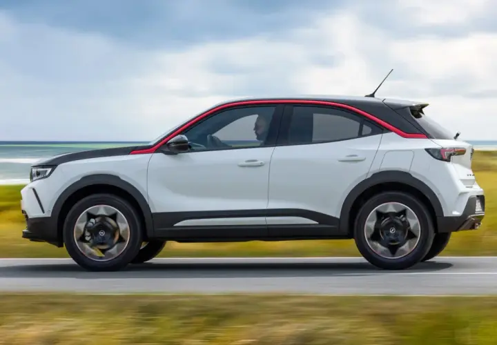 Opel Mokka blanco con detalles rojos, conduciendo por la costa. Las opiniones sobre este coche son muy positivas.