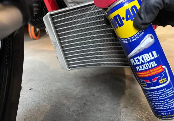 Mano enguantada usa spray WD-40 para limpiar radiador coche.