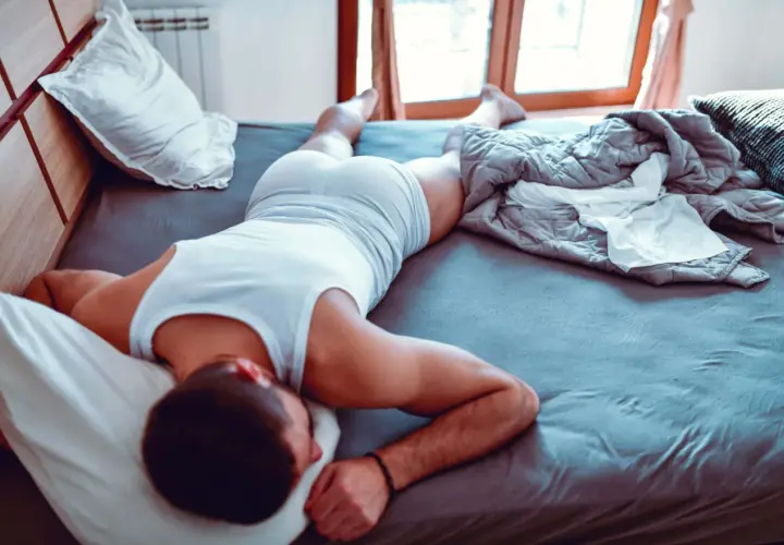Hombre durmiendo en la cama, con una camiseta blanca y pantalones cortos. Se siente cómodo, es bueno dormir sin ropa interior.