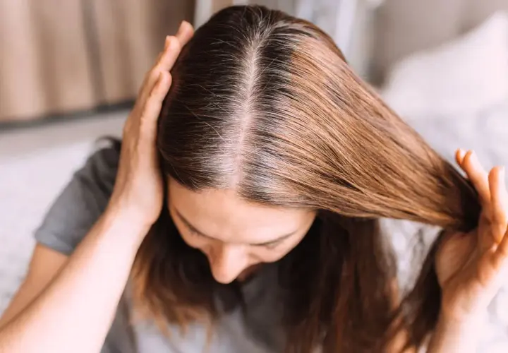 Una joven se toca el cabello, mostrando mechones grises. Se pregunta: "porque me salen canas si soy joven".