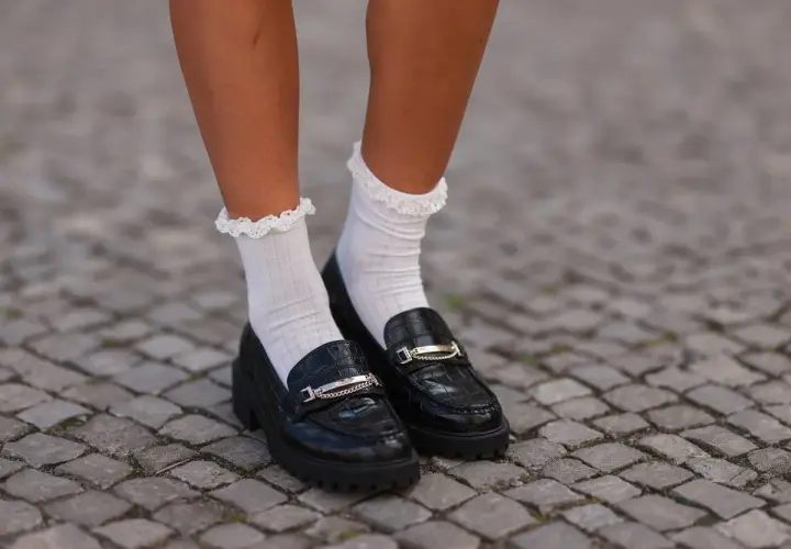 Mocasines negros con detalle de cadena y calcetines blancos con volantes. Un look moderno y chic.