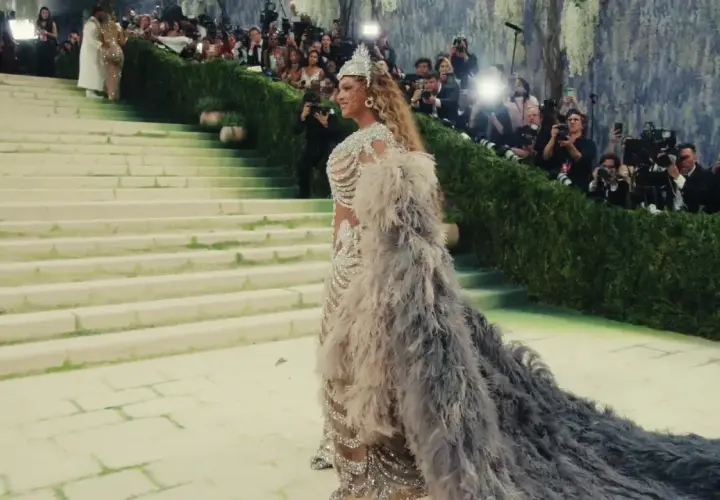 Una mujer desciende escaleras con un vestido de plumas y pedrería, rodeada de fotógrafos. Es un momento icónico de cuando es la Met Gala.