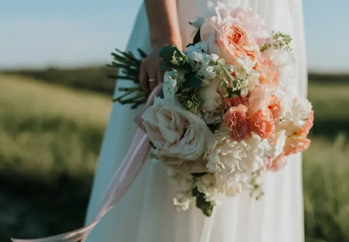 Novia con ramo de flores en tonos pastel, la última tendencia en ramos de novia, con cintas rosas cayendo.