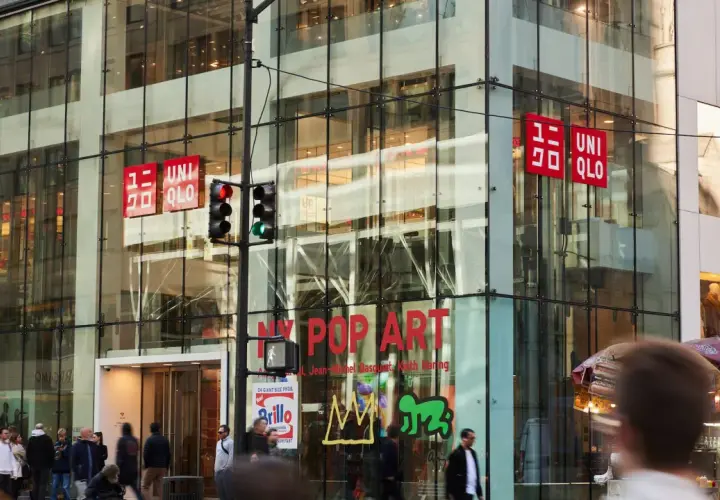 Edificio de cristal con letreros rojos de UNIQLO. La tienda, de origen japonés, se encuentra en una calle concurrida.