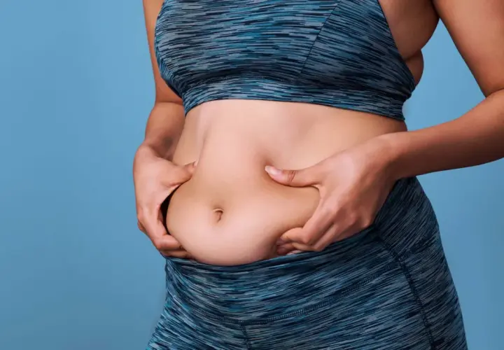 Mujer de 50 años se pellizca el abdomen, buscando perder grasa abdominal.