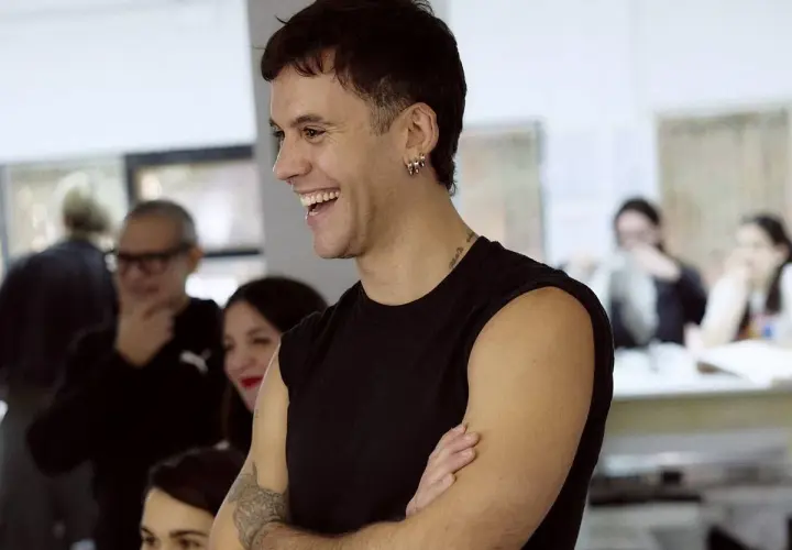 Luis de Javier diseñador, sonriente y con los brazos cruzados, rodeado de gente en un taller.