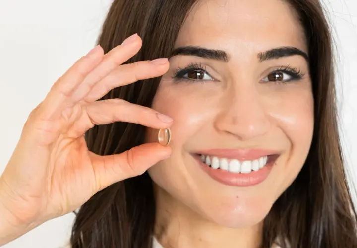 Mujer sonriente muestra una cápsula de omega 7, un aliado para quienes buscan adelgazar de forma natural.