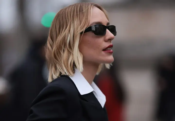 Mujer con melena corta rubia, gafas de sol y traje negro. Cortes de pelo melena corta modernos y chic.
