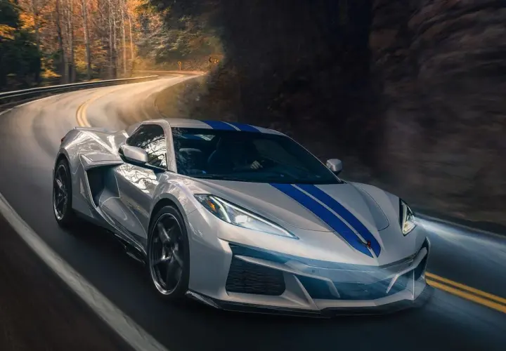 Un deportivo plateado con franjas azules recorre una carretera sinuosa entre árboles. Podría ser el mejor coche del mundo.