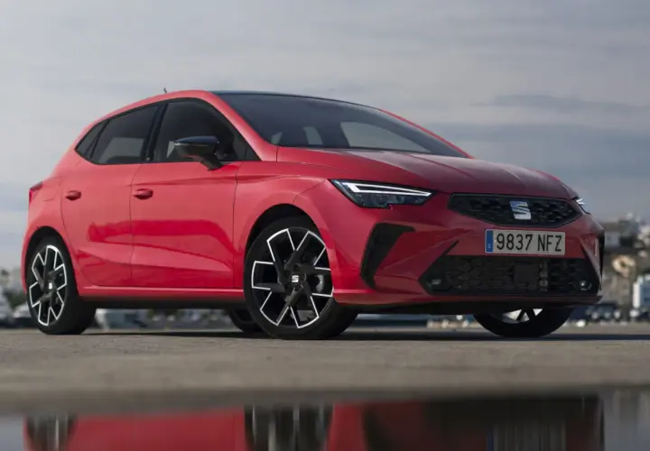 Un Seat Ibiza rojo vibrante, uno de los modelos más icónicos, posa con estilo frente a un paisaje urbano.